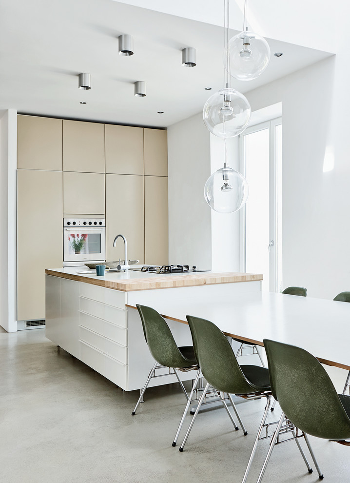 Mid-sized modern eat-in kitchen in Hamburg with flat-panel cabinets, beige cabinets, wood benchtops, concrete floors, with island, a drop-in sink and stainless steel appliances.