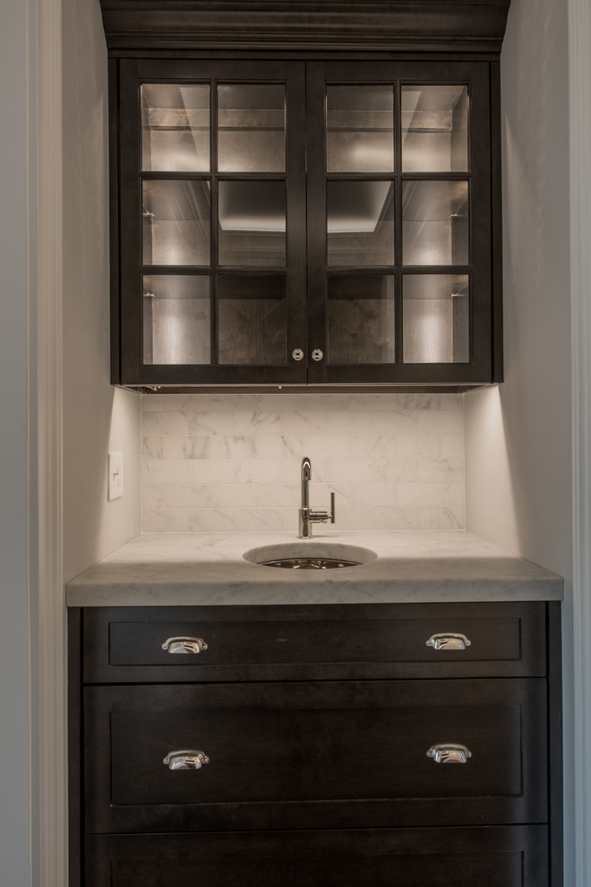 Mid-sized traditional galley wet bar in Bridgeport with an undermount sink, shaker cabinets, dark wood cabinets, marble benchtops, white splashback, marble splashback, dark hardwood floors and brown floor.