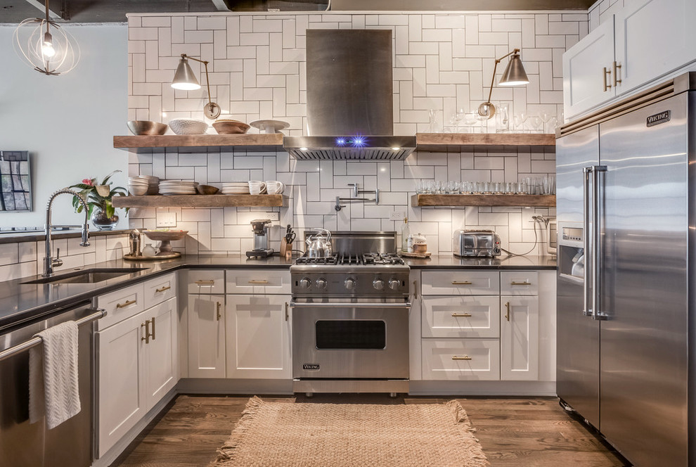 This is an example of an industrial kitchen in Atlanta with an undermount sink, shaker cabinets, white cabinets, white splashback, stainless steel appliances, medium hardwood floors and a peninsula.