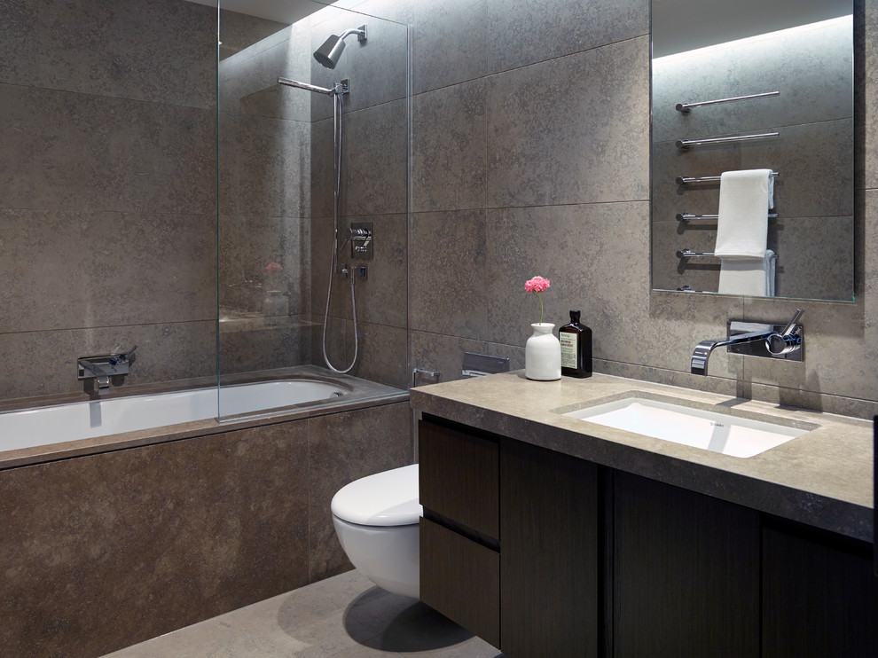 Photo of a mid-sized contemporary master bathroom in London with flat-panel cabinets, dark wood cabinets, a drop-in tub, a shower/bathtub combo, a wall-mount toilet, beige tile, porcelain tile, beige walls, limestone floors, a drop-in sink and limestone benchtops.