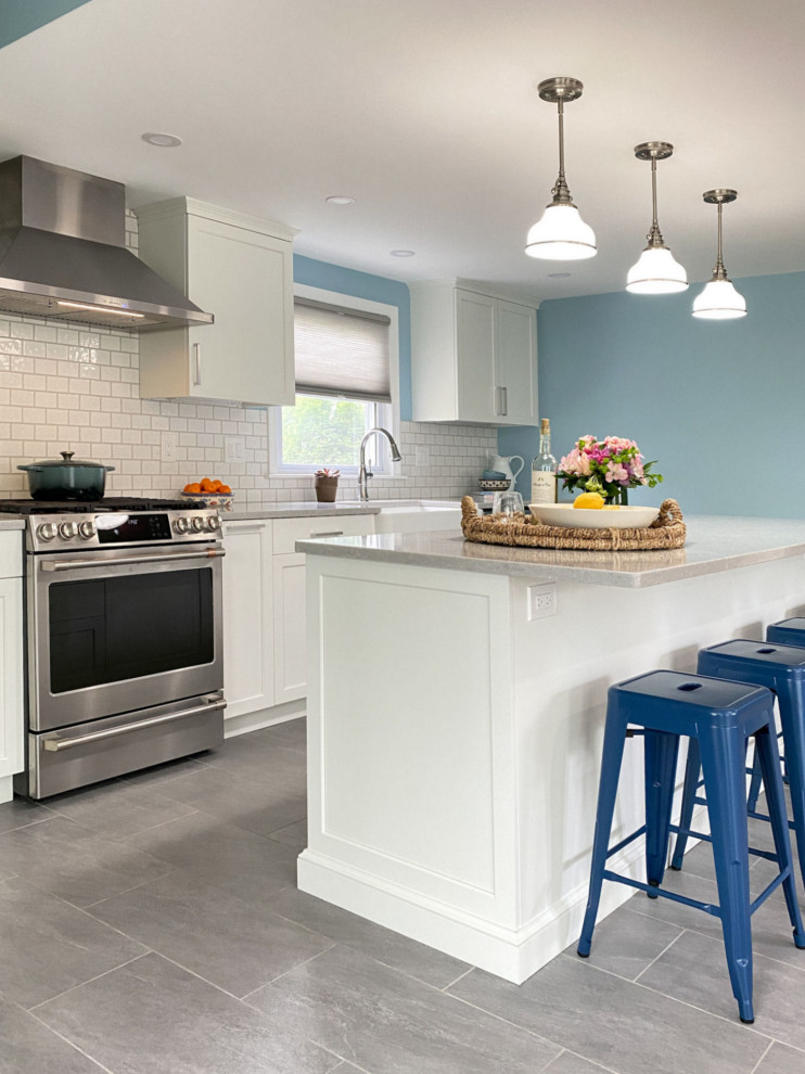 Inspiration for a classic kitchen/diner in Boston with a belfast sink, raised-panel cabinets, white cabinets, engineered stone countertops, white splashback, ceramic splashback, stainless steel appliances, porcelain flooring, an island, grey floors and white worktops.