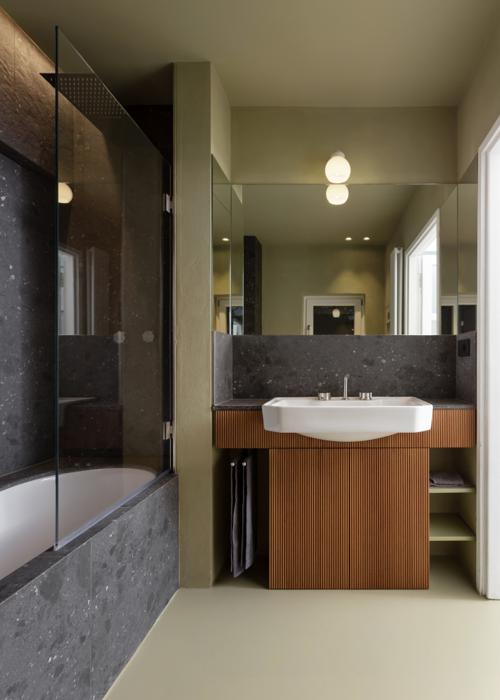 Cette image montre une petite salle d'eau vintage avec un placard avec porte à panneau surélevé, des portes de placard marrons, une baignoire encastrée, un combiné douche/baignoire, WC séparés, un carrelage noir, des carreaux de porcelaine, un mur vert, sol en béton ciré, une vasque, un plan de toilette en carrelage, un sol vert, une cabine de douche à porte battante, un plan de toilette noir, une niche, meuble simple vasque, meuble-lavabo encastré et un plafond décaissé.