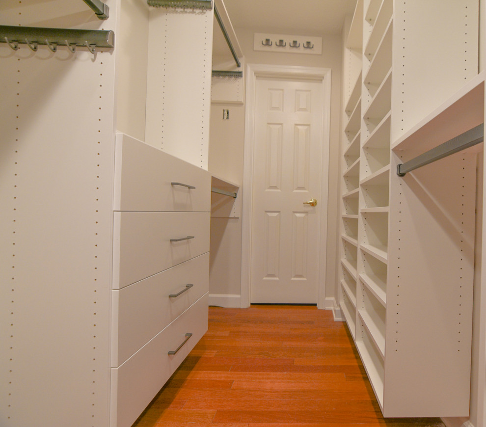 Photo of a mid-sized traditional gender-neutral walk-in wardrobe in Other with flat-panel cabinets, white cabinets, medium hardwood floors, brown floor and vaulted.