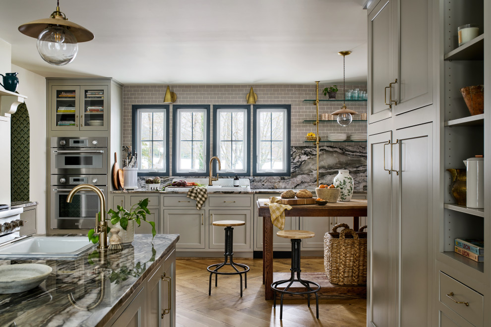 Eat-in kitchen - large transitional l-shaped medium tone wood floor and brown floor eat-in kitchen idea in Baltimore with gray backsplash, stainless steel appliances, two islands, gray countertops, a drop-in sink, recessed-panel cabinets, gray cabinets, marble countertops and marble backsplash