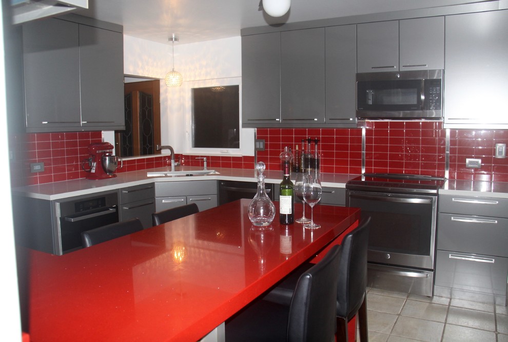 Photo of a mid-sized modern u-shaped eat-in kitchen in Hawaii with an undermount sink, flat-panel cabinets, grey cabinets, quartz benchtops, red splashback, glass tile splashback, stainless steel appliances, ceramic floors and a peninsula.