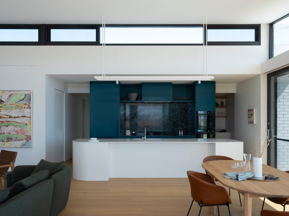 This is an example of a galley open plan kitchen in Other with an undermount sink, flat-panel cabinets, blue cabinets, limestone benchtops, blue splashback, marble splashback, light hardwood floors, with island and white benchtop.