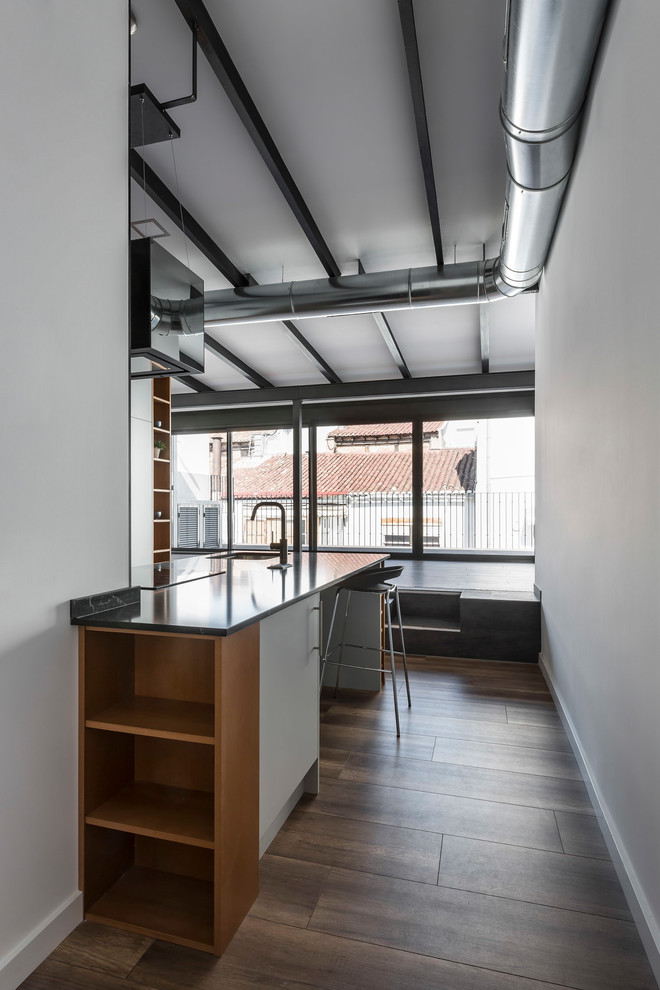 Diseño de cocina comedor urbana con fregadero bajoencimera, armarios abiertos, puertas de armario blancas, salpicadero metalizado, salpicadero de metal, electrodomésticos con paneles, suelo laminado, península y encimeras negras