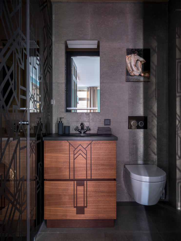 Design ideas for a small transitional powder room in Moscow with flat-panel cabinets, medium wood cabinets, a wall-mount toilet, gray tile, limestone, grey walls, limestone floors, an undermount sink, granite benchtops, grey floor and black benchtops.