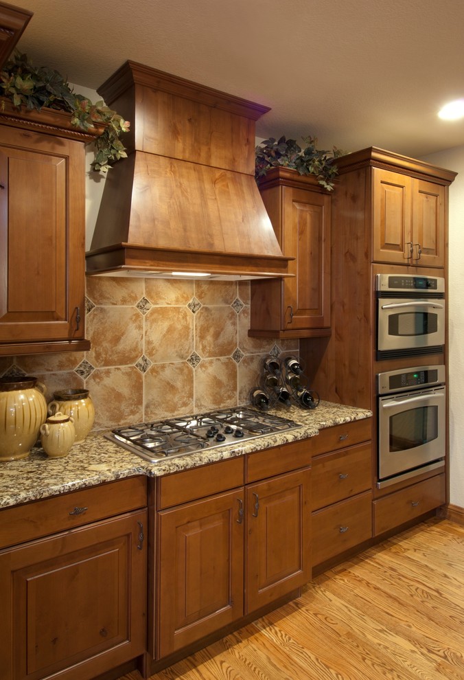 This is an example of a mid-sized arts and crafts u-shaped eat-in kitchen in Denver with a double-bowl sink, raised-panel cabinets, medium wood cabinets, granite benchtops, multi-coloured splashback, ceramic splashback, stainless steel appliances, medium hardwood floors and a peninsula.