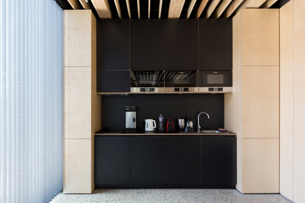 Photo of a small contemporary single-wall kitchen in Other with a drop-in sink, flat-panel cabinets, black cabinets, black splashback, panelled appliances, terrazzo floors, no island, grey floor and black benchtop.
