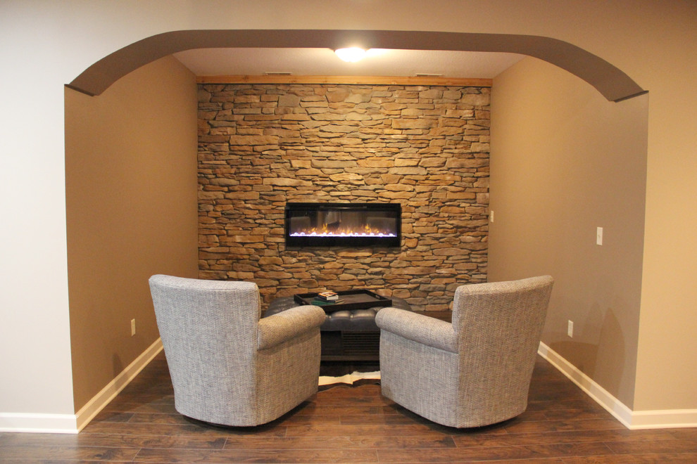 Large mountain style underground laminate floor and brown floor basement photo with beige walls, a standard fireplace and a stone fireplace