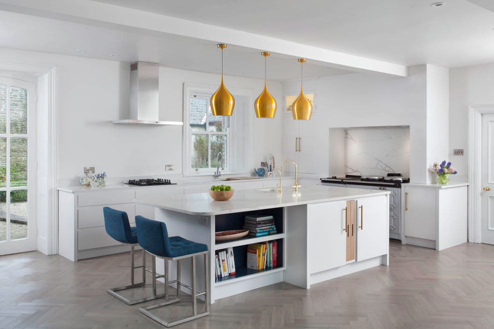 This is an example of a contemporary l-shaped kitchen in Dublin with an undermount sink, flat-panel cabinets, white cabinets, white splashback, stone slab splashback, light hardwood floors, with island and white benchtop.