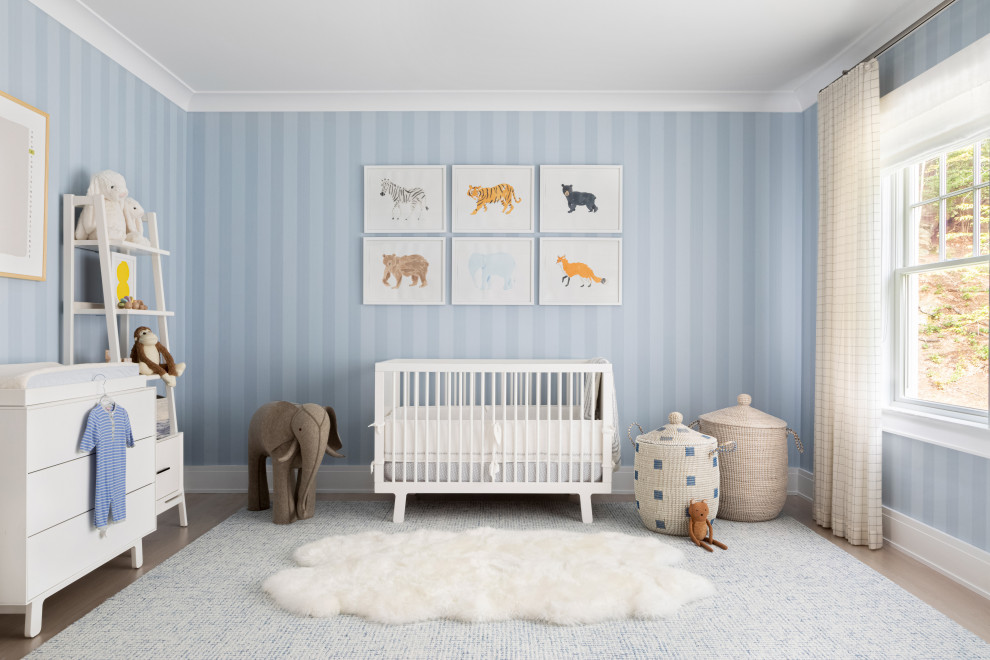 Large traditional nursery in New York with blue walls, light hardwood floors and brown floor for boys.