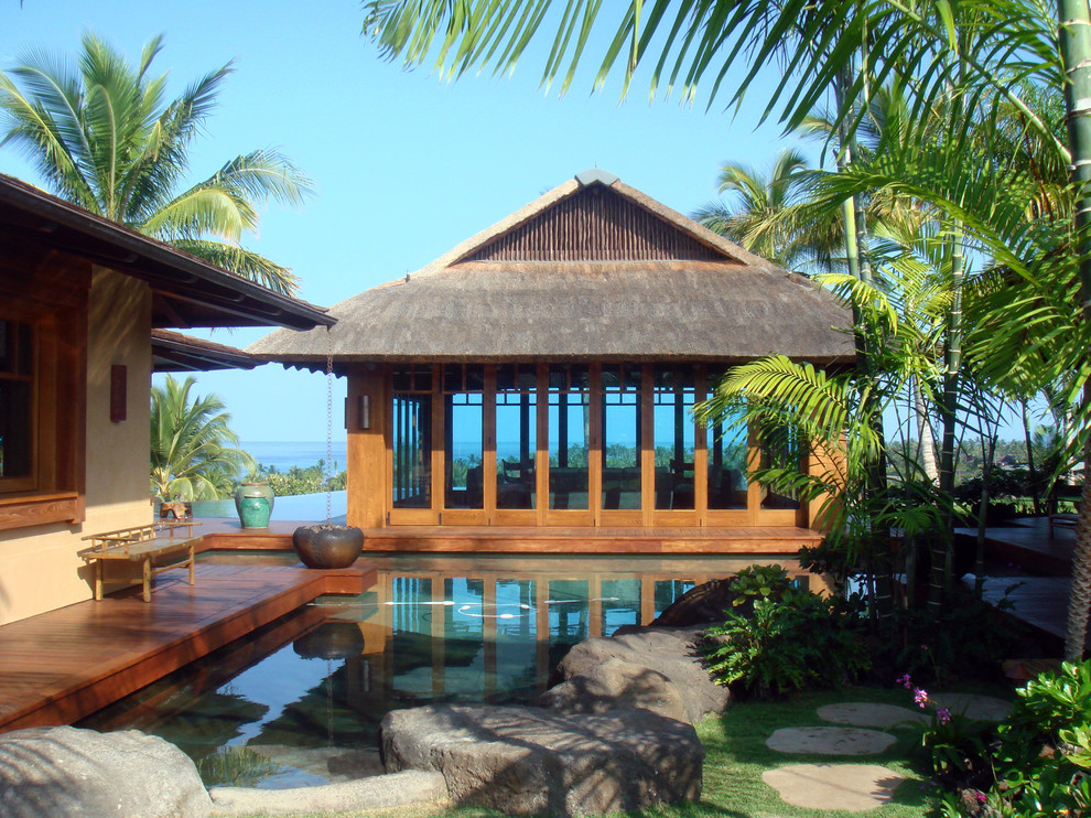 Photo of a tropical backyard custom-shaped natural pool in Hawaii with a pool house and decking.