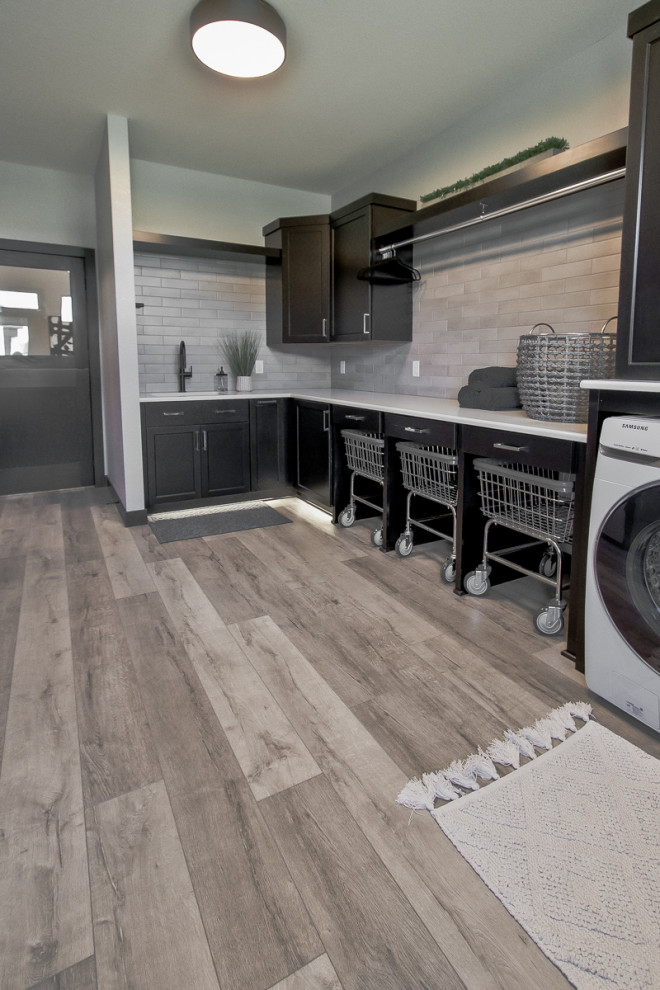 Photo of a transitional laundry room in Other with recessed-panel cabinets, dark wood cabinets, ceramic splashback, vinyl floors, grey floor, white splashback and a side-by-side washer and dryer.