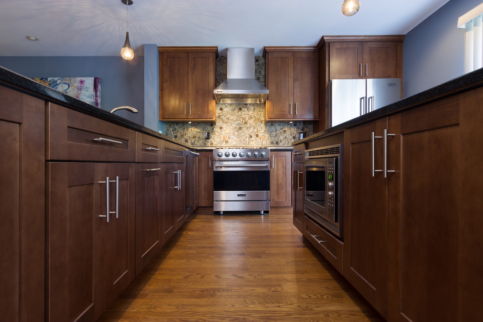 This is an example of a mid-sized transitional l-shaped separate kitchen in Chicago with a double-bowl sink, shaker cabinets, medium wood cabinets, multi-coloured splashback, mosaic tile splashback, stainless steel appliances, medium hardwood floors, with island, granite benchtops, blue floor and brown benchtop.