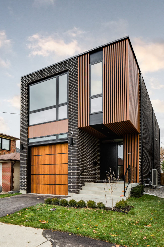 This is an example of a small contemporary two-storey brick black house exterior in Toronto with a flat roof and board and batten siding.