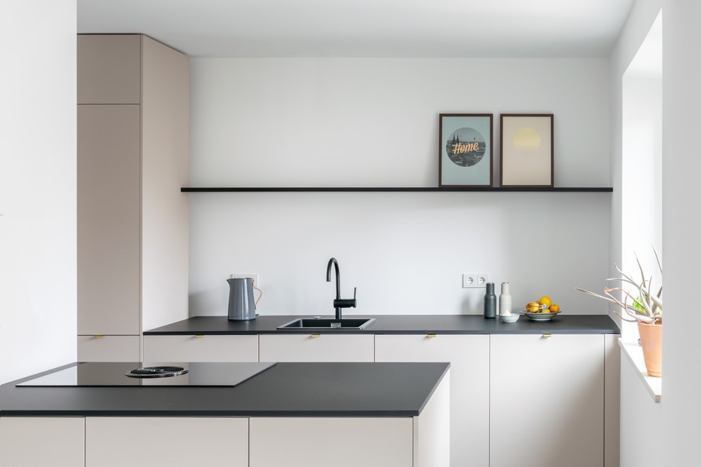 Photo of a mid-sized contemporary single-wall open plan kitchen in Munich with a drop-in sink, flat-panel cabinets, beige cabinets, quartz benchtops, white splashback, black appliances, concrete floors, with island, grey floor and black benchtop.