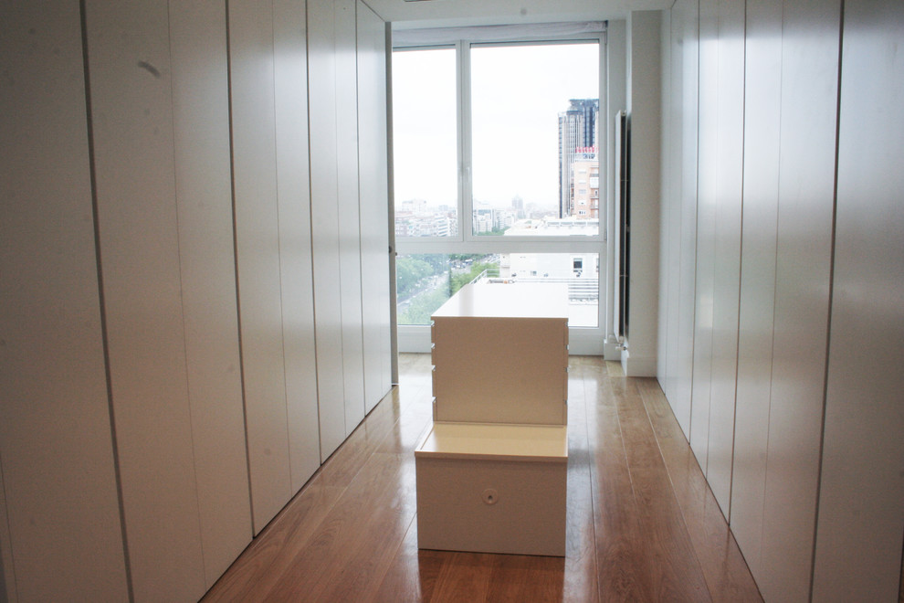 Imagen de armario vestidor unisex tradicional renovado grande con armarios con paneles lisos, puertas de armario blancas y suelo de madera en tonos medios