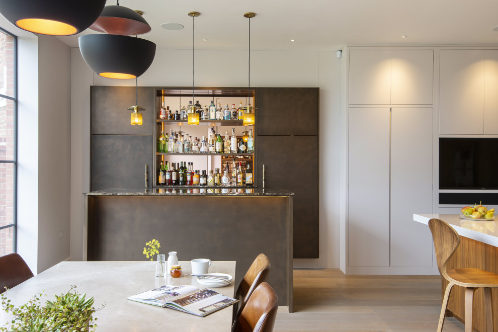Mid-sized contemporary galley home bar in London with flat-panel cabinets, quartzite benchtops, grey cabinets, mirror splashback, beige floor and grey benchtop.