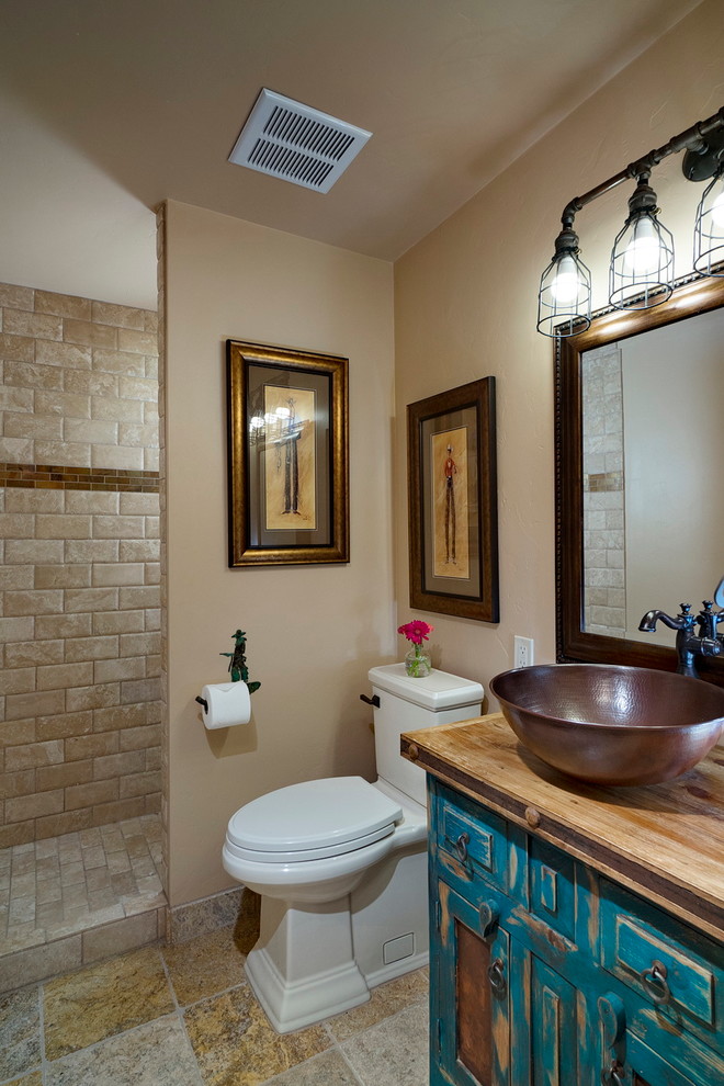 Example of a small mountain style 3/4 beige tile and porcelain tile porcelain tile doorless shower design in Phoenix with furniture-like cabinets, distressed cabinets, a one-piece toilet, beige walls, a vessel sink and wood countertops