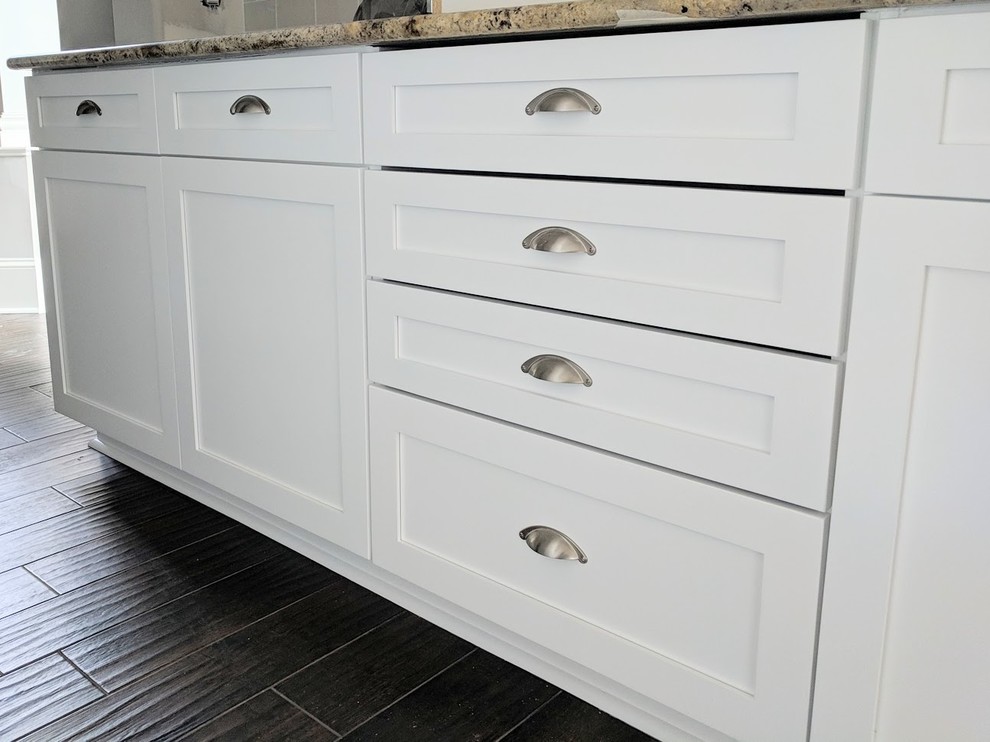Inspiration for a mid-sized transitional porcelain tile and brown floor open concept kitchen remodel with a farmhouse sink, shaker cabinets, white cabinets, granite countertops, white backsplash, ceramic backsplash, stainless steel appliances and an island