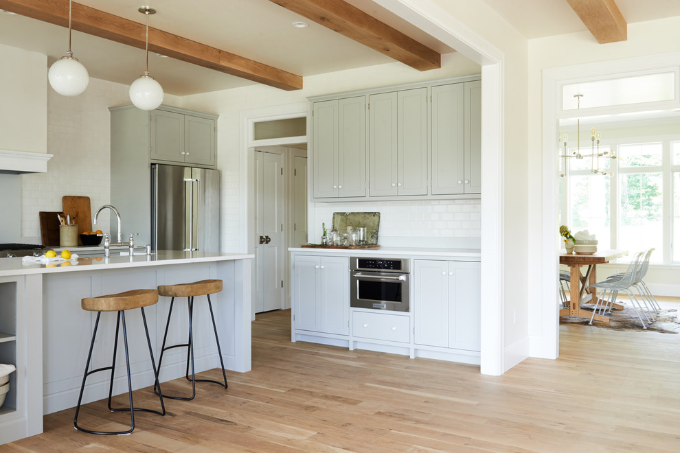 Open concept kitchen - mid-sized transitional l-shaped light wood floor and brown floor open concept kitchen idea with shaker cabinets, gray cabinets, white backsplash, subway tile backsplash, stainless steel appliances and an island