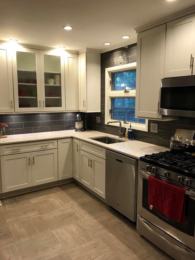 Mid-sized transitional l-shaped eat-in kitchen in New York with an undermount sink, shaker cabinets, white cabinets, granite benchtops, grey splashback, stainless steel appliances and grey floor.