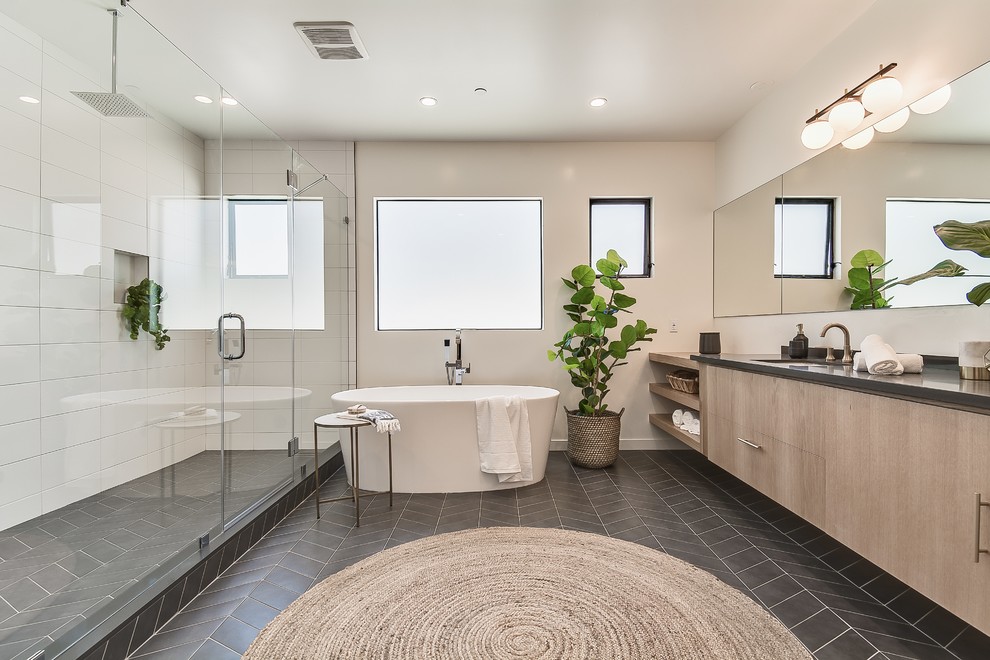 Design ideas for a large beach style master bathroom in Los Angeles with flat-panel cabinets, light wood cabinets, white tile, ceramic tile, ceramic floors, granite benchtops, black floor, a hinged shower door, a freestanding tub, an alcove shower, beige walls, an undermount sink and black benchtops.