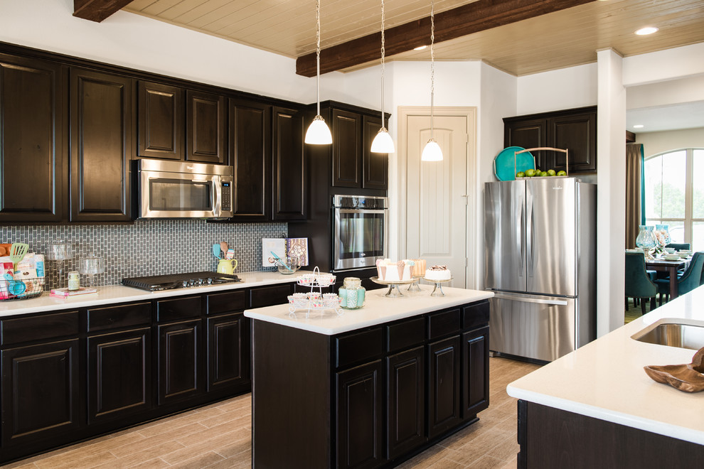 Eat-in kitchen - large transitional porcelain tile eat-in kitchen idea in Austin with a single-bowl sink, raised-panel cabinets, dark wood cabinets, quartzite countertops, gray backsplash, glass tile backsplash, stainless steel appliances and an island