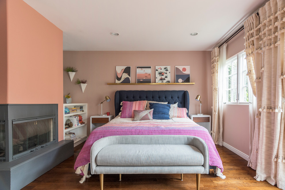 Transitional master bedroom in Los Angeles with pink walls, medium hardwood floors, a corner fireplace, a plaster fireplace surround and brown floor.