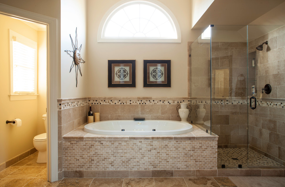 This is an example of a traditional master bathroom in Charlotte with an integrated sink, raised-panel cabinets, medium wood cabinets, granite benchtops, a drop-in tub, a corner shower, beige tile, stone tile, beige walls, limestone floors and a two-piece toilet.