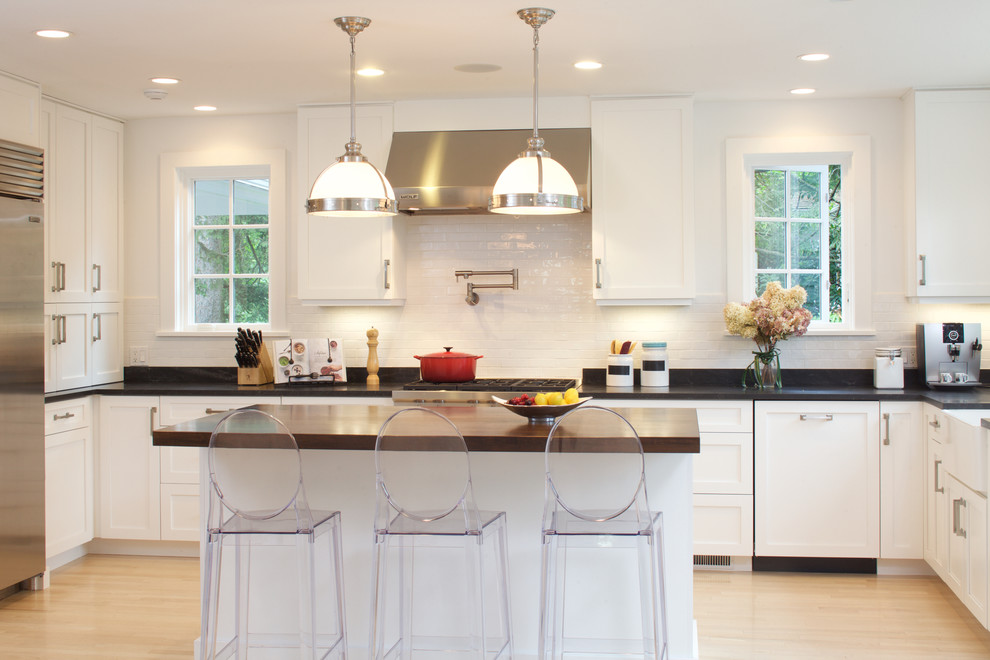 Eat-in kitchen - mid-sized transitional l-shaped light wood floor eat-in kitchen idea in New York with a farmhouse sink, shaker cabinets, white cabinets, granite countertops, white backsplash, subway tile backsplash, stainless steel appliances and an island