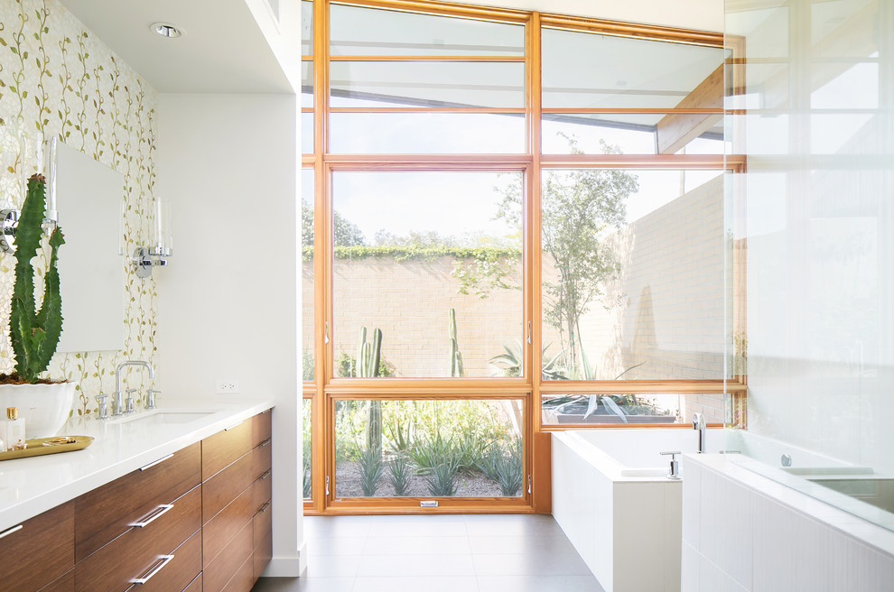 Midcentury master bathroom in Phoenix with medium wood cabinets, an undermount tub, multi-coloured tile, glass tile, white walls, flat-panel cabinets, an undermount sink, grey floor and white benchtops.