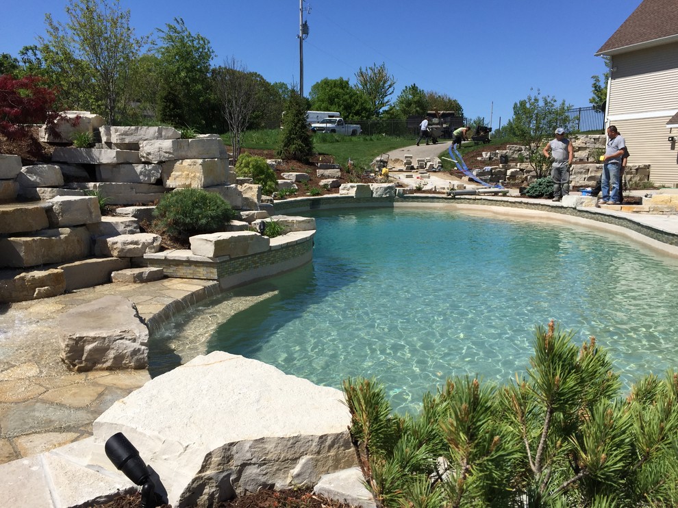 Inspiration for an expansive modern backyard custom-shaped natural pool in Grand Rapids with a water feature and natural stone pavers.
