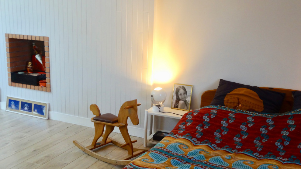 Aménagement d'une petite chambre mansardée ou avec mezzanine grise et jaune éclectique avec un mur blanc, parquet clair, cheminée suspendue, un sol beige et du lambris de bois.
