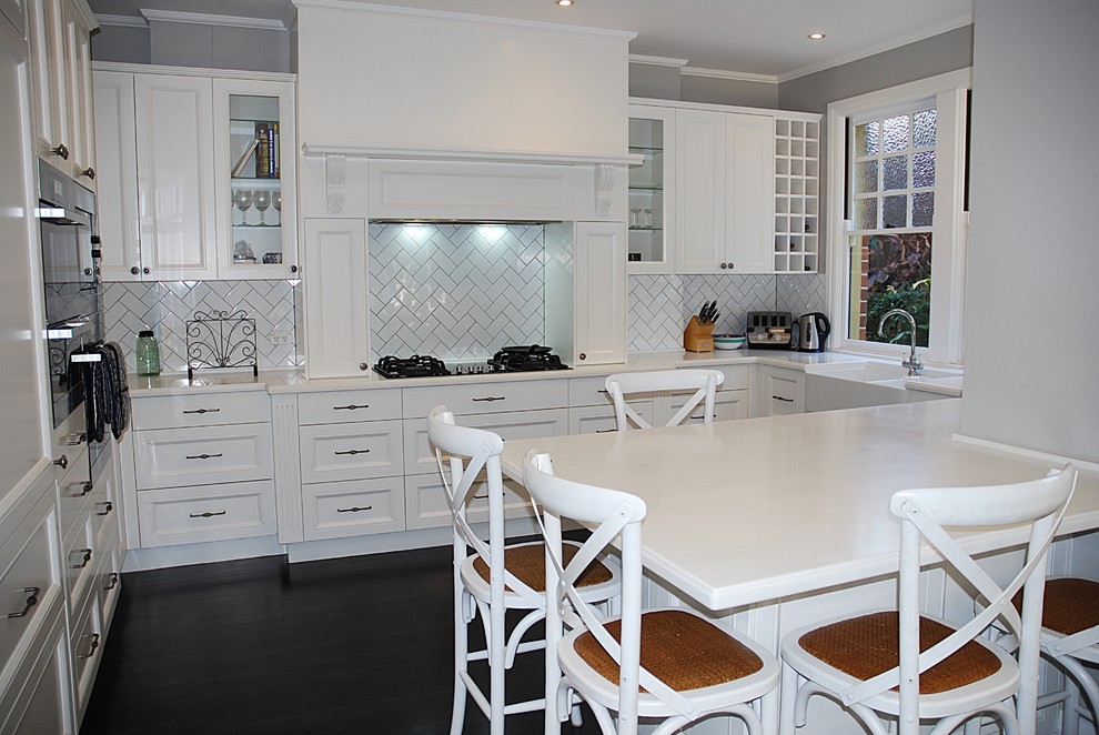 Inspiration for a large traditional u-shaped eat-in kitchen in Sydney with a farmhouse sink, shaker cabinets, white cabinets, solid surface benchtops, white splashback, subway tile splashback, stainless steel appliances, dark hardwood floors and no island.