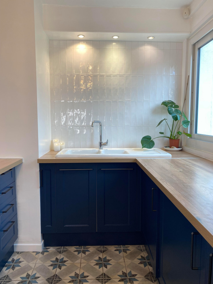 Foto på ett stort retro brun kök, med en undermonterad diskho, luckor med infälld panel, blå skåp, träbänkskiva, vitt stänkskydd, stänkskydd i keramik, integrerade vitvaror, cementgolv och blått golv