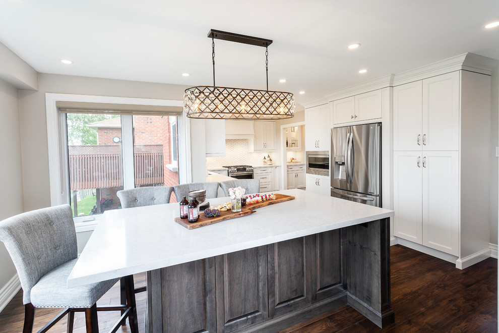 Large transitional u-shaped dark wood floor and brown floor eat-in kitchen photo in Toronto with an undermount sink, recessed-panel cabinets, white cabinets, quartz countertops, white backsplash, ceramic backsplash, stainless steel appliances, an island and white countertops