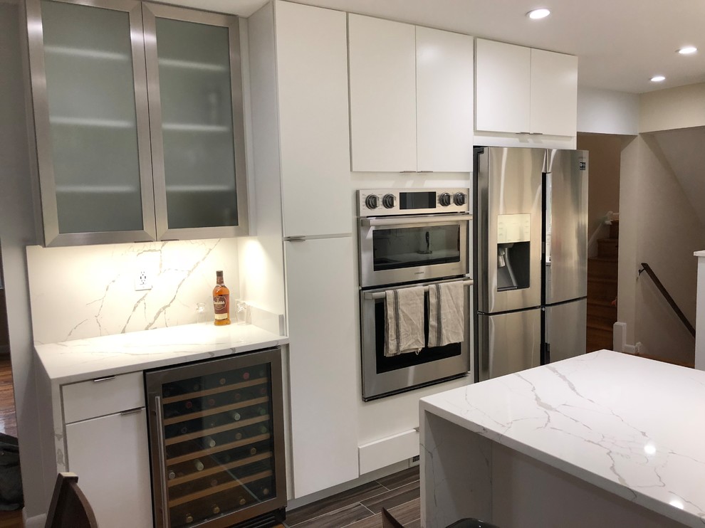 Expansive contemporary u-shaped eat-in kitchen in DC Metro with an undermount sink, flat-panel cabinets, white cabinets, quartz benchtops, white splashback, stone slab splashback, stainless steel appliances, porcelain floors, a peninsula, brown floor and white benchtop.