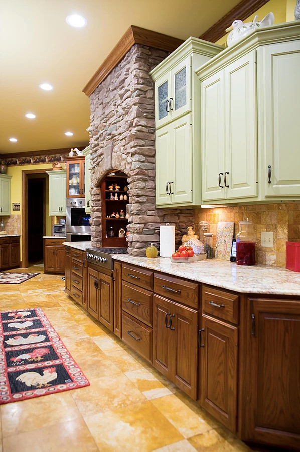 Example of a large mountain style u-shaped porcelain tile and beige floor eat-in kitchen design with an undermount sink, raised-panel cabinets, green cabinets, granite countertops, beige backsplash, porcelain backsplash, stainless steel appliances, an island and multicolored countertops