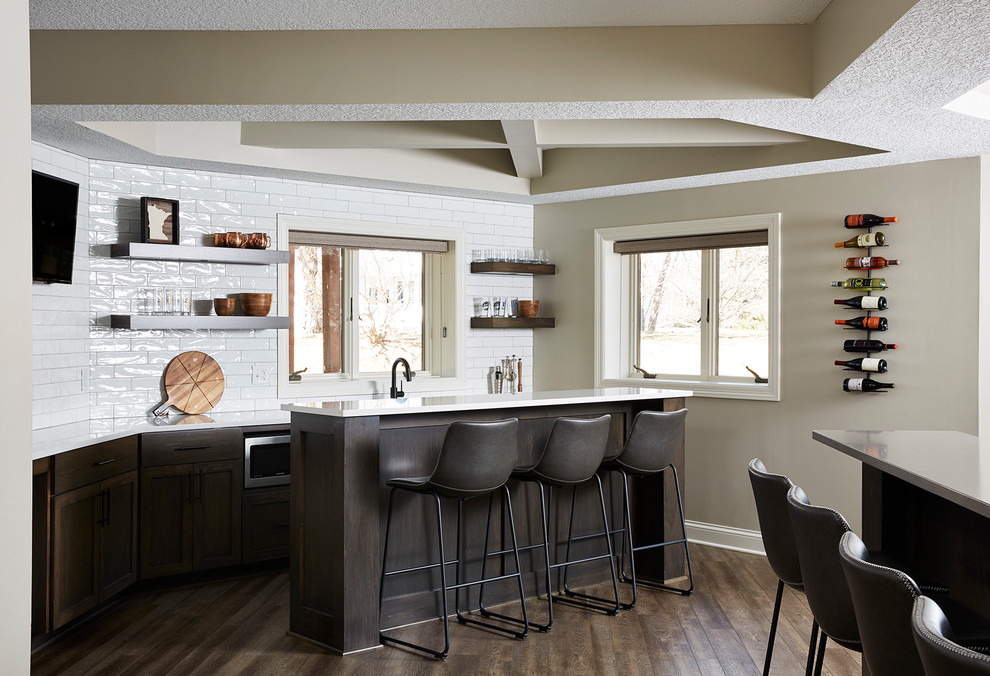 Design ideas for a mid-sized transitional galley wet bar in Minneapolis with an undermount sink, recessed-panel cabinets, dark wood cabinets, quartz benchtops, white splashback, subway tile splashback, vinyl floors, brown floor and white benchtop.