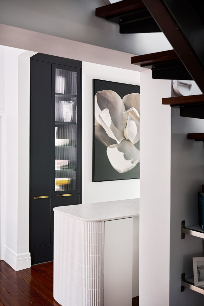 Example of a large minimalist galley dark wood floor and brown floor kitchen design in Perth with an undermount sink, flat-panel cabinets, white cabinets, quartz countertops, white backsplash, quartz backsplash, black appliances, an island and white countertops