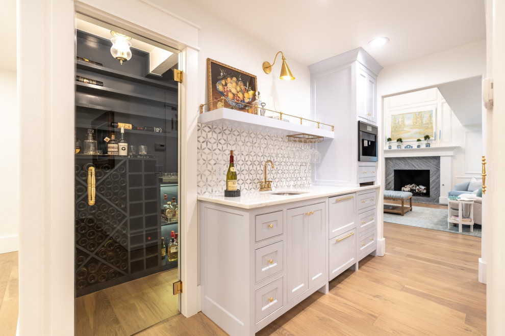 Mid-sized traditional single-wall wet bar in Oklahoma City with an undermount sink, flat-panel cabinets, blue cabinets, marble benchtops, blue splashback, marble splashback, light hardwood floors and white benchtop.