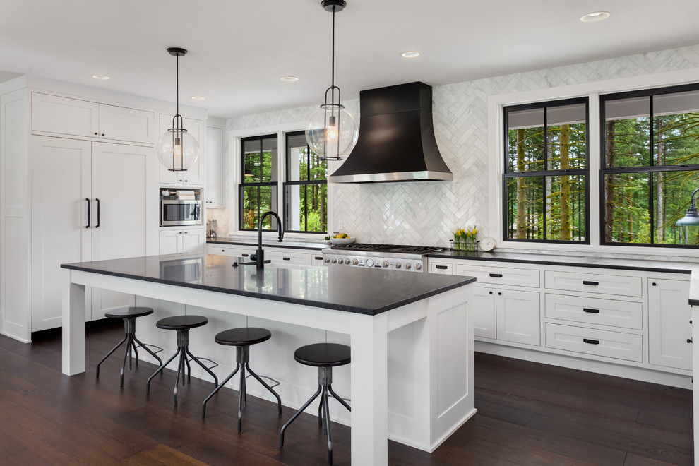 Inspiration for a transitional l-shaped dark wood floor and brown floor kitchen remodel in DC Metro with a farmhouse sink, shaker cabinets, white backsplash, paneled appliances, an island and black countertops