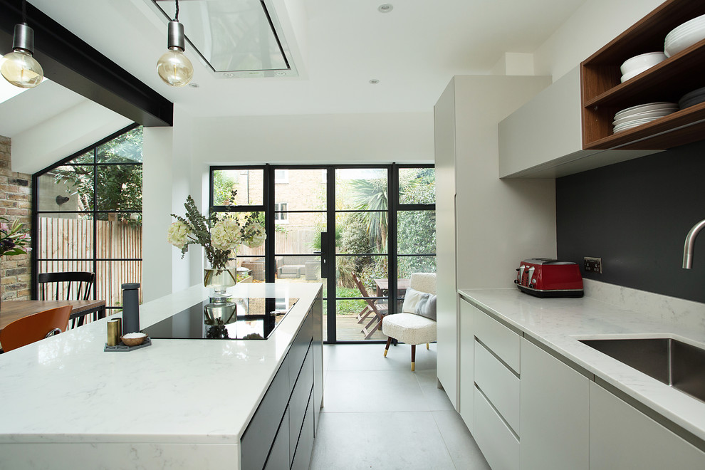This is an example of a contemporary galley eat-in kitchen in London with an undermount sink, flat-panel cabinets, white cabinets, white splashback, panelled appliances, with island, white floor and white benchtop.
