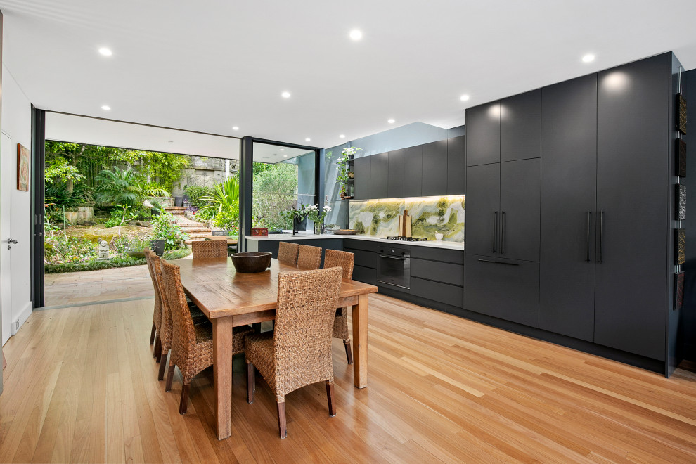 Photo of a contemporary l-shaped eat-in kitchen in Sydney with an undermount sink, black cabinets, quartz benchtops, green splashback, marble splashback, black appliances, medium hardwood floors, no island, white benchtop, flat-panel cabinets and brown floor.