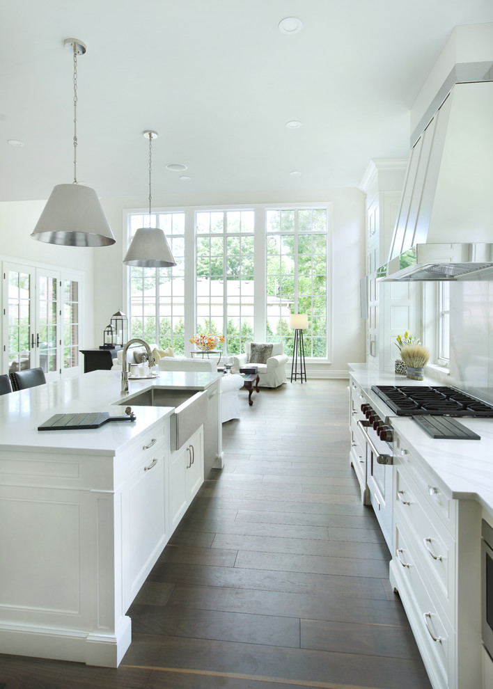 Inspiration for a large transitional l-shaped open plan kitchen in Toronto with recessed-panel cabinets, white cabinets, white splashback, porcelain splashback, dark hardwood floors, with island, white benchtop, a farmhouse sink, stainless steel appliances and brown floor.
