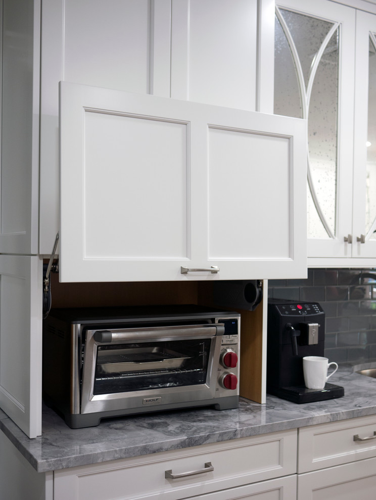 Inspiration for a mid-sized transitional l-shaped medium tone wood floor eat-in kitchen remodel in New York with an undermount sink, shaker cabinets, white cabinets, quartzite countertops, gray backsplash, glass tile backsplash, stainless steel appliances and a peninsula