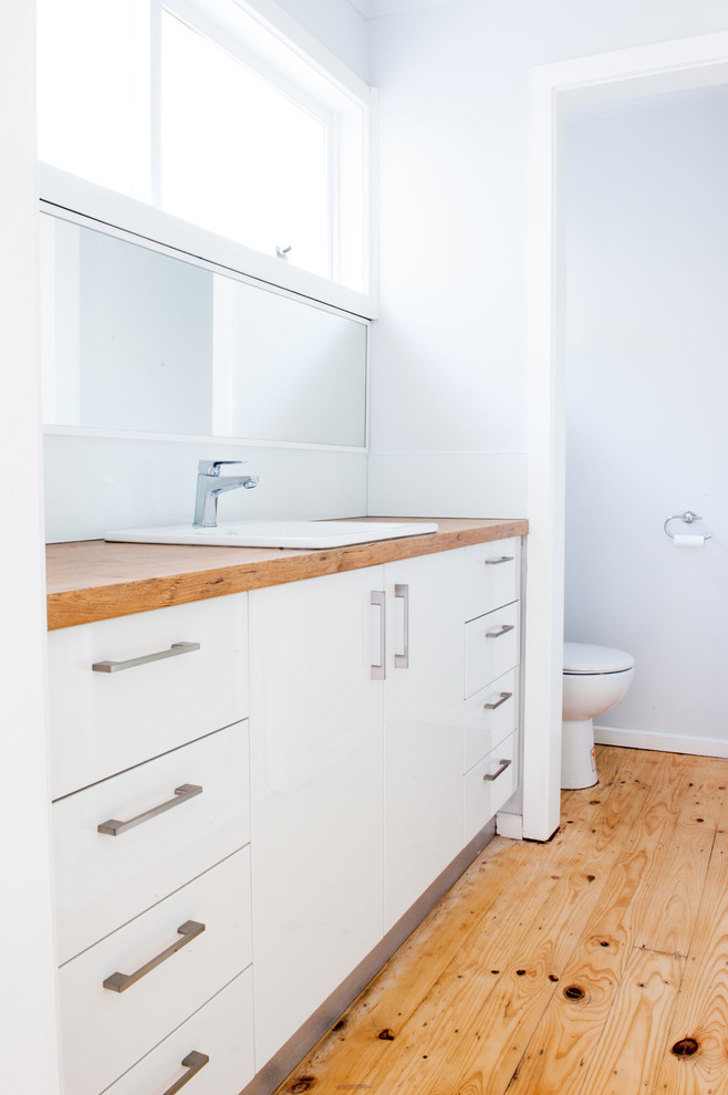 This is an example of a mid-sized traditional bathroom in Melbourne with open cabinets, white cabinets, a one-piece toilet, white tile, cement tile, white walls, light hardwood floors, a drop-in sink and wood benchtops.